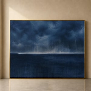 May include: A rectangular landscape painting in a thin gold frame featuring a dark navy blue sea under a stormy, textured sky. A thin, bright horizontal line of light separates the dark water from the heavy, rain-filled clouds above.