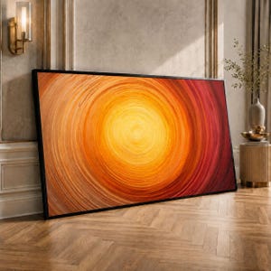 May include: A framed abstract artwork with a spiral pattern in orange, yellow, and red hues. The piece is leaning against a wall, with a wooden floor. The artwork's dimensions are not visible.