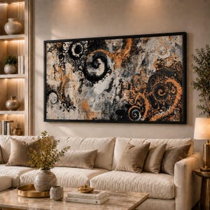 May include: Abstract wall art with a black frame. The artwork features swirling patterns in black, orange, and white against a neutral background. The painting hangs above a beige sofa with brown throw pillows, creating a cozy living room setting.