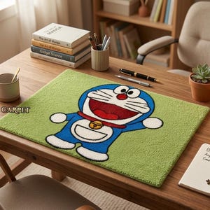 May include: A green rectangular rug featuring a cartoon image of Doraemon, a blue cat-like robot character with a red collar and a bell. The rug is on a wooden desk with books, pens, and a small potted plant.