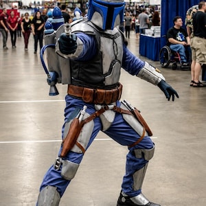 May include: A full-body costume featuring a silver and blue helmet with a T-shaped visor, a silver chest plate, a blue jumpsuit, and a jetpack. The outfit includes a brown utility belt, silver leg armor, and black boots, with a blaster held forward.