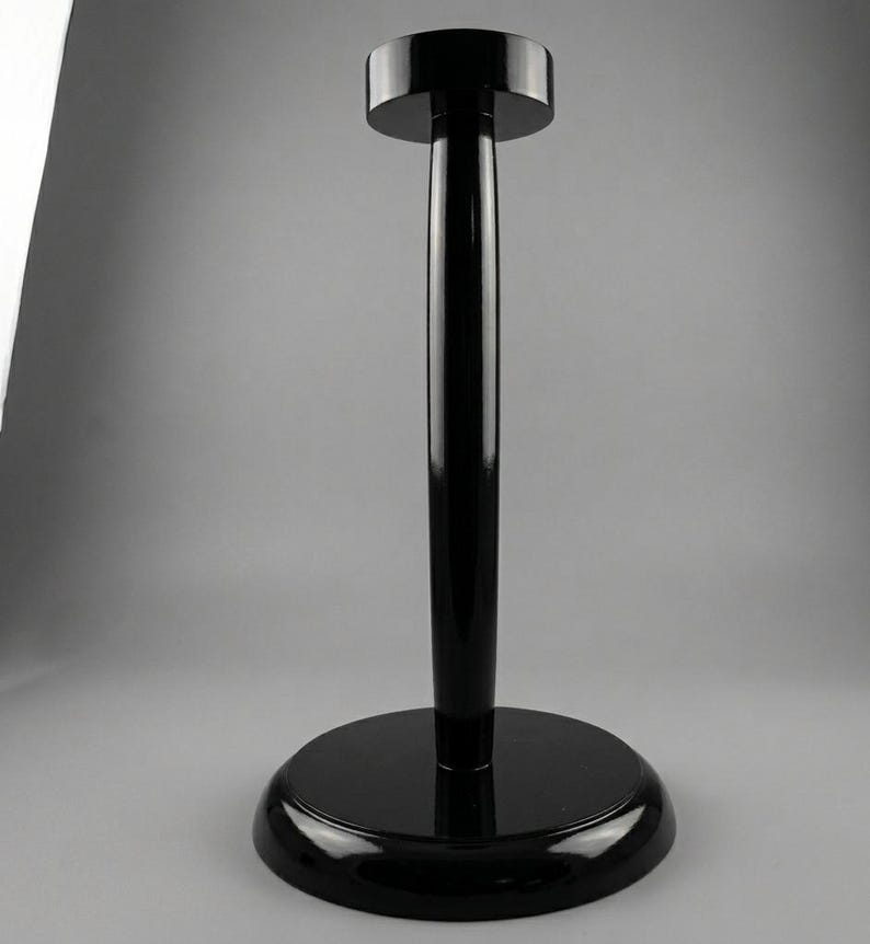 May include: A glossy black hat stand with a circular base and a cylindrical pole. The top of the stand is a smaller, circular platform. The stand is made of a shiny, reflective material.