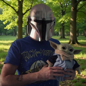May include: A person wearing a silver Mandalorian helmet and a blue t-shirt with "Rick and Morty" text. The person is holding a Grogu plush toy wearing a blue jacket with a tan collar. The background is a green park.