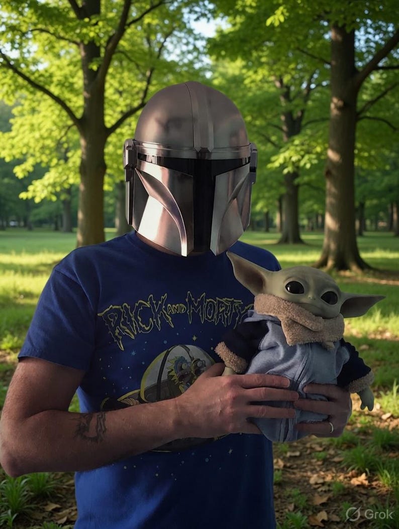 May include: A person wearing a silver Mandalorian helmet and a blue t-shirt with "Rick and Morty" text. The person is holding a Grogu plush toy wearing a blue jacket with a tan collar. The background is a green park.