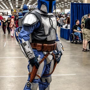 May include: A full-body Mandalorian-style costume featuring a silver and blue helmet with a T-shaped visor, silver chest and limb armor, a blue jumpsuit, a brown leather utility belt, and a jetpack with blue accents worn over the shoulders.