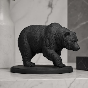 Könnte beinhalten: Eine mattschwarze Bärenfigur auf einem runden Sockel. Der Bär ist in einer schreitenden Pose dargestellt, mit detaillierter Fellstruktur, sichtbaren Ohren und einer nach vorne gerichteten Schnauze. Die Skulptur ist durchgehend einfarbig schwarz.