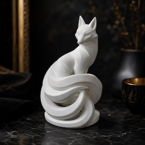 Può includere: Una scultura bianco opaco di una volpe con code multiple e curve. La volpe è raffigurata in posizione seduta con la testa leggermente girata di lato. La superficie della statuetta mostra sottili linee di trama su tutta la forma dell'animale.
