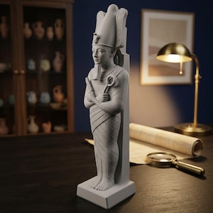 May include: A matte light grey statue of an Egyptian pharaoh standing on a rectangular base. The figure wears a traditional tall crown and a false beard, with arms crossed over the chest holding a crook and flail, set against a dark background.