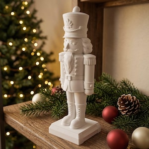 Könnte beinhalten: Eine mattweiße Nussknacker-Figur auf einem rechteckigen Sockel. Die Soldatenfigur zeigt einen hohen Hut mit Blattemblem, eine detaillierte Uniform mit Epauletten, einen Bart und Stiefel mit Schnürung, alles in einer einheitlich weißen Ausführung.