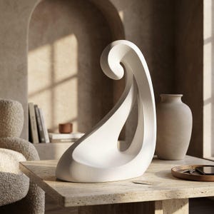 Peut inclure: Une sculpture abstraite blanche avec une forme incurvée et lisse rappelant une vague, dotée d'un espace central ouvert. L'objet présente une finition mate avec de fines lignes de texture horizontales sur toute sa structure.