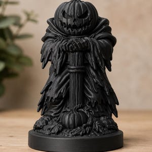 Könnte beinhalten: Eine mattschwarze Figur einer verhüllten Gestalt mit einem geschnitzten Kürbiskopf, die mit verschränkten Armen auf einem hohen Stab steht. Die Figur befindet sich auf einem runden Sockel, umgeben von kleinen Kürbissen und Blättern.