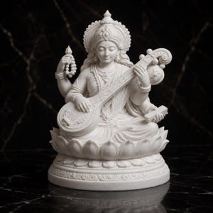 Peut inclure: Une statue blanche de la divinité Saraswati assise sur une base en forme de fleur de lotus. La figure possède quatre bras, tenant un chapelet dans une main et un instrument de musique veena sur les genoux, portant des bijoux et une couronne.