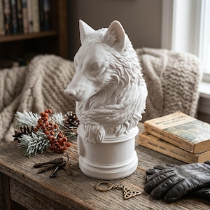 Könnte beinhalten: Eine weiße Wolfsbüsten-Skulptur mit detaillierter Fellstruktur und einem um den Hals gewickelten Schal, montiert auf einem zylindrischen Sockel. Die Skulptur ist in mattem Weiß gehalten und zeigt fein ausgearbeitete Gesichtszüge des Tieres.