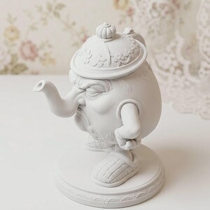 May include: A matte white anthropomorphic teapot figurine featuring a round body, a curved spout, and a lid with floral relief details. The character has a grumpy facial expression, articulated arms, and wears textured slippers while standing on a base.