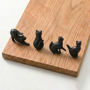 May include: Four small, black, cast metal cat-shaped knobs or hooks arranged in a row. Each piece features a distinct feline pose, including one stretching, one sitting upright, one sitting with a raised paw, and one sitting with a curved tail.