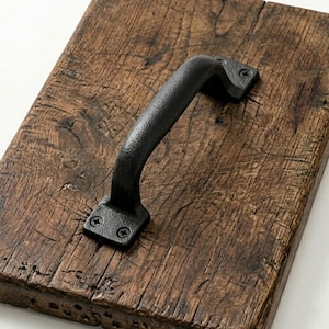 Könnte beinhalten: Ein rustikales Serviertablett aus Holz mit einem schwarzen Metallgriff. Das Tablett besteht aus Altholz mit sichtbarer Maserung und Astlöchern. Der Griff ist mit Schrauben befestigt und hat eine strukturierte Oberfläche.
