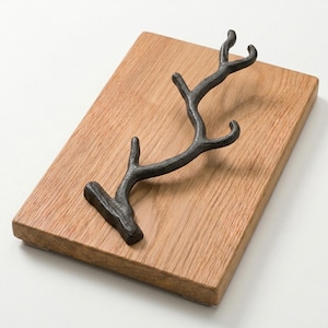 Puede incluir: Un gancho de pared de hierro fundido gris oscuro con forma de rama de árbol con múltiples puntas, montado sobre una tabla de madera rectangular de color marrón claro con un patrón de veta natural visible y acabado mate texturizado.