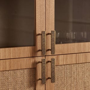May include: A light oak wood cabinet featuring four doors with vertical rectangular brass handles. The upper doors have glass panels, while the lower doors are inset with woven cane mesh. The cabinet has a natural wood grain finish throughout.