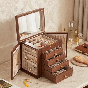 May include: A dark wood jewelry box with a hinged lid featuring an interior mirror, two side-opening doors with hooks for necklaces, and four pull-out drawers. The interior is lined with cream fabric and includes compartments for rings and earrings.