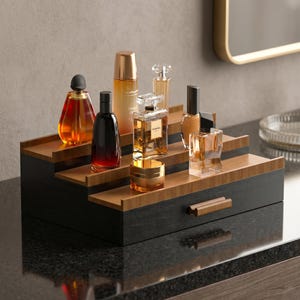 May include: A tiered, black and bamboo-toned organiser displaying various perfume bottles and cosmetic containers. The organiser has a small drawer with a wooden handle. The bottles are in various shapes and sizes, with amber, clear, and black glass.