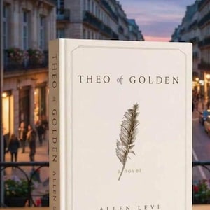 May include: A hardcover book titled "THEO of GOLDEN" by Allen Levi. The book has a cream-colored cover with a feather illustration and the words "a novel". The spine reads "THEO of GOLDEN ALLEN LEVI". The background shows a European street scene.