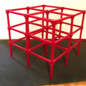 Puede incluir: Una estructura de escalada geométrica roja brillante para niños. Está hecha de tubos interconectados que forman una forma de cubo con múltiples niveles y una base estable. Diseño simple y funcional, adecuado para jugar en interiores o exteriores.