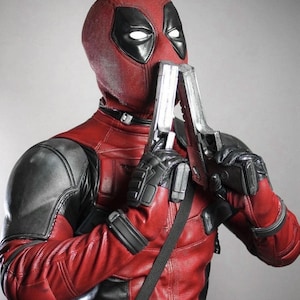 Puede incluir: Un disfraz de Deadpool rojo y negro con una m&aacute;scara y dos pistolas de juguete plateadas. El disfraz presenta un body rojo con detalles negros, un cintur&oacute;n negro y guantes negros. La m&aacute;scara tiene ojos blancos.