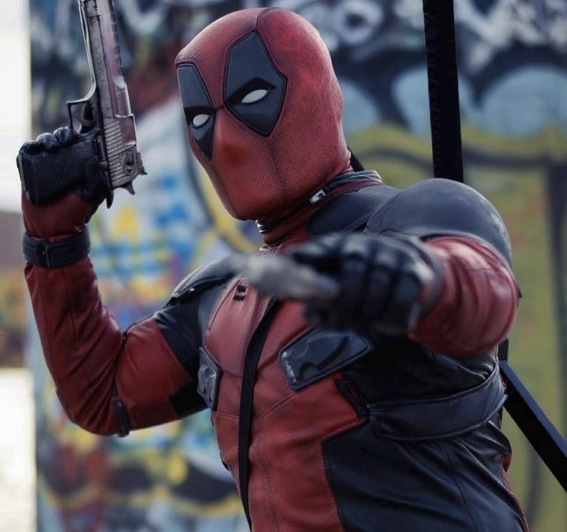 Puede incluir: Una persona con un disfraz de Deadpool, vistiendo un traje rojo y negro con una m&aacute;scara. La persona sostiene una pistola plateada en su mano derecha y una cuchilla en su mano izquierda. El fondo presenta arte de graffiti.