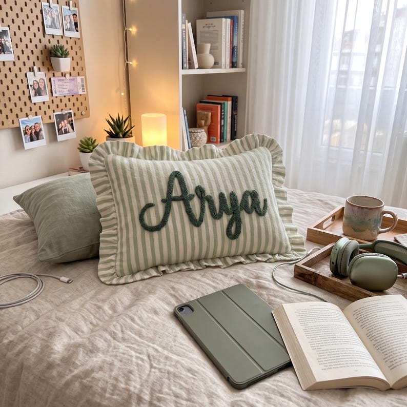 a cozy bedroom scene with a bed, a pillow with the name "Arya" embroidered on it, a laptop, a book, and some other personal items.