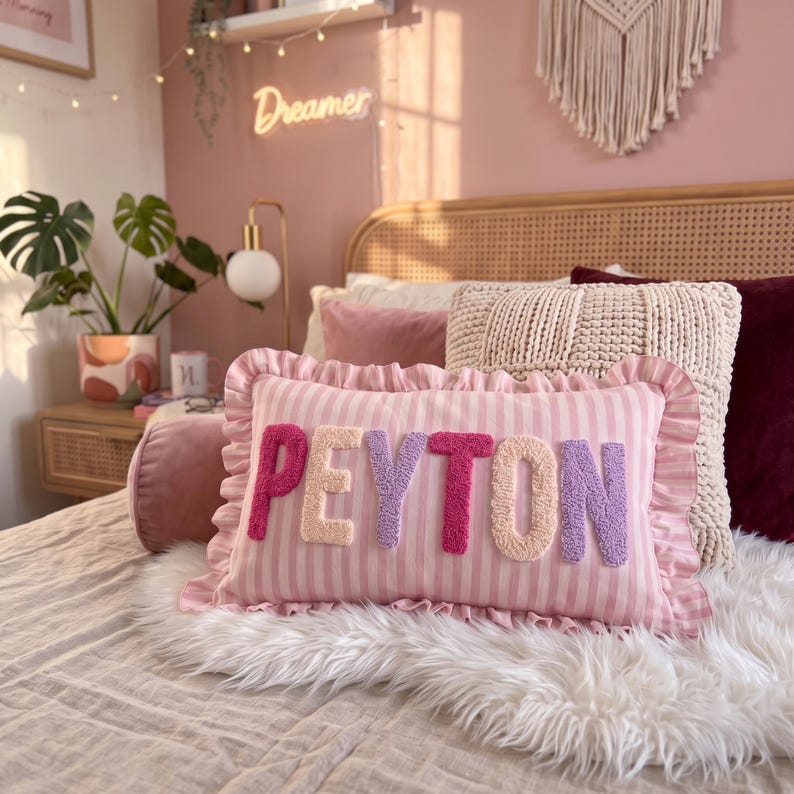 A bedroom with a pink and white striped pillow that says "Peyton" in pink and purple letters, along with other pillows and decorative items.