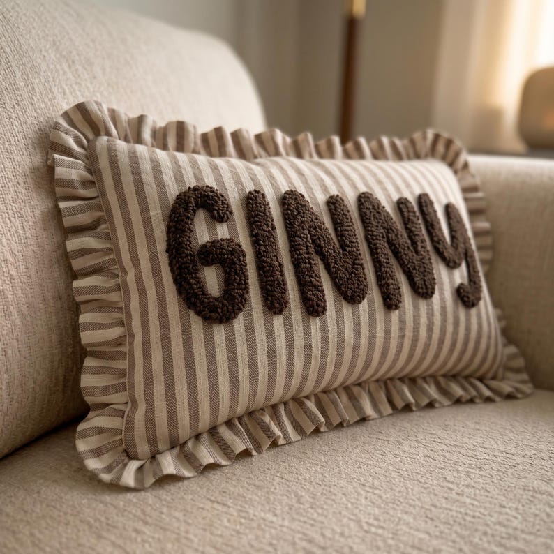 A decorative pillow with the word "GINNY" embossed on it, sitting on a beige couch.