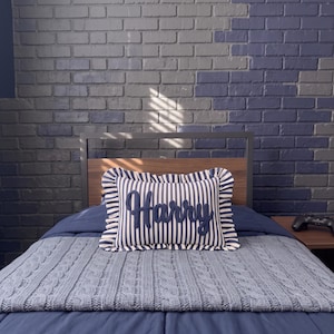 a bedroom with a bed, a pillow with the name "Harry" on it, and a brick wall in the background.