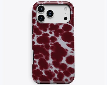 Puede incluir: Una funda para smartphone con un patrón moteado de color rojo oscuro y blanco, similar a manchas de tinta. La funda tiene un recorte rectangular para las lentes de la cámara y el flash. La palabra KUKA está impresa en la parte inferior.
