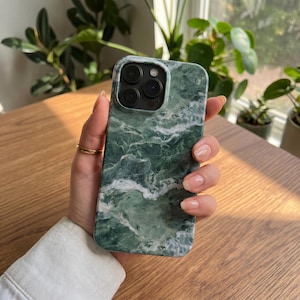 May include: A smartphone case featuring a dark green and white marble pattern with a glossy finish. The case has a square cutout at the top left corner for the camera lenses and is designed to fit a device with a triple camera system.