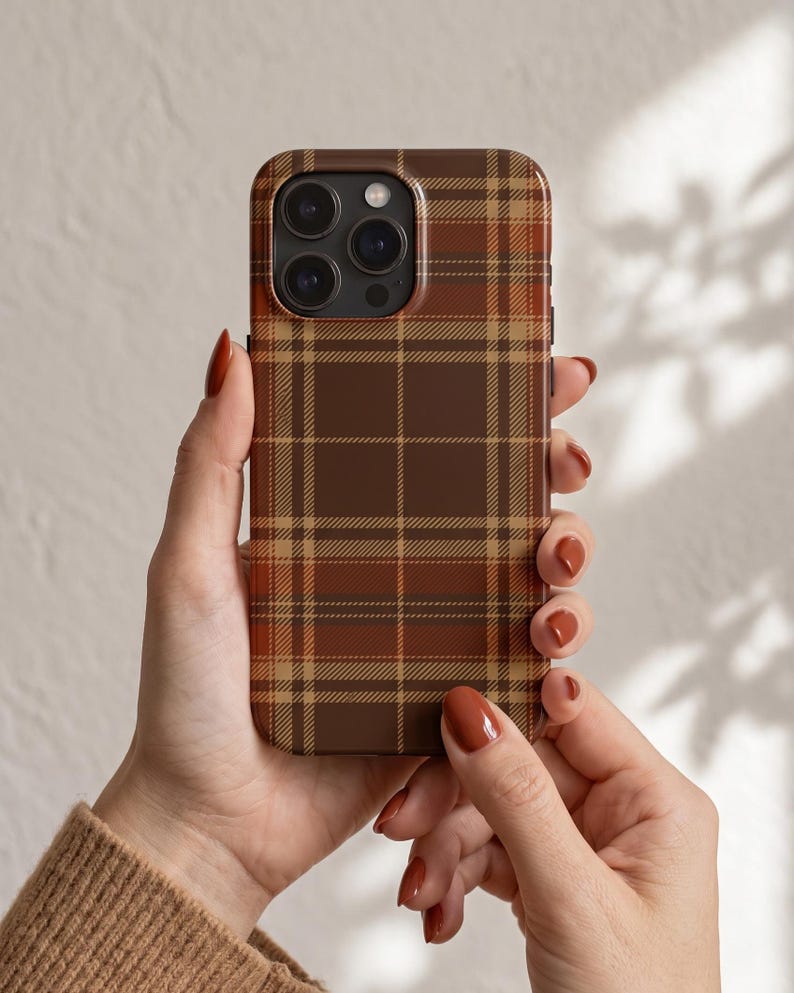 Puede incluir: Una funda para smartphone con un patr&oacute;n de cuadros en tonos marr&oacute;n, beige y naranja oscuro. El dise&ntilde;o consiste en l&iacute;neas horizontales y verticales que se cruzan formando una cuadr&iacute;cula de tart&aacute;n cl&aacute;sica en toda la parte trasera.