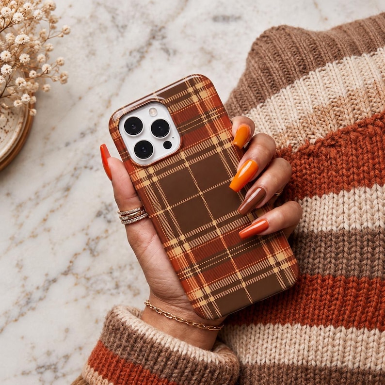 Puede incluir: Una funda para smartphone con un patr&oacute;n de cuadros en marr&oacute;n, naranja y crema con un recorte cuadrado para la c&aacute;mara. La funda tiene un acabado liso, cubre la parte trasera y los laterales del dispositivo y muestra un dise&ntilde;o de cuadr&iacute;cula.