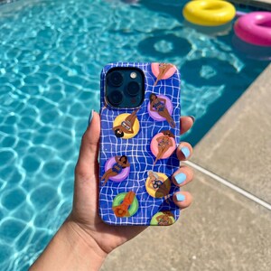 May include: A smartphone case featuring a blue swimming pool tile pattern with illustrations of various figures floating on colorful circular pool rings. The design includes multiple people in swimwear relaxing on yellow, pink, purple, and green floats.