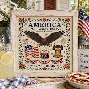Op de afbeelding: Kruissteekkunstwerk in een verweerde witte lijst, ter viering van de 250e verjaardag van Amerika. Het ontwerp toont een adelaar, de Amerikaanse vlag, de Liberty Bell en de tekst "AMERICA 250th ANNIVERSARY 1776-2026". Het kunstwerk is omgeven door bloemen- en stermotieven.