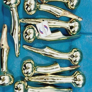 Könnte beinhalten: Eine Sammlung von nautischen Griffen aus poliertem Messing mit abgerundeten Enden und Montagelöchern. Die Beschläge haben eine reflektierende goldfarbene Oberfläche und enthalten ein kleines weißes rechteckiges Etikett mit dem in Blau und Rot gedruckten Text ALFA NAUTICAL.