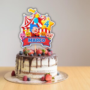 Puede incluir: Una tarta de cumplea&ntilde;os con un adorno decorativo con una carpa de circo, personajes de dibujos animados y el nombre "MARCO" en una pancarta roja. La tarta est&aacute; cubierta con fresas frescas, ar&aacute;ndanos y moras, y tiene glaseado de chocolate.