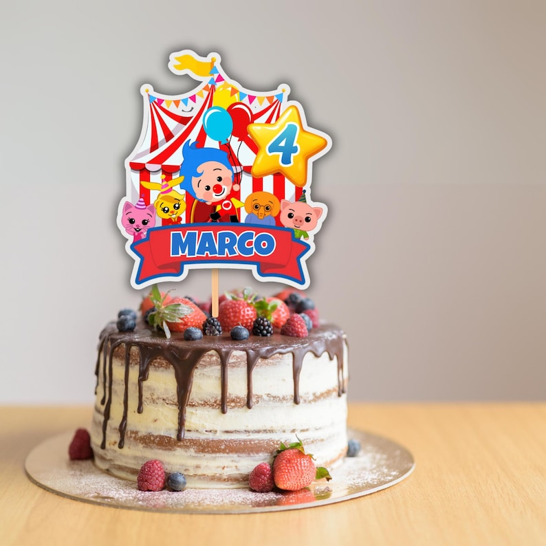 Puede incluir: Una tarta de cumplea&ntilde;os con un adorno decorativo con una carpa de circo, personajes de dibujos animados y el nombre "MARCO" en una pancarta roja. La tarta est&aacute; cubierta con fresas frescas, ar&aacute;ndanos y moras, y tiene glaseado de chocolate.