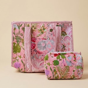 May include: A quilted tote bag and a matching small zippered pouch, both featuring a pink base with a multi-coloured botanical print of flowers and leaves in shades of green, red, and white, finished with a red and white striped fabric trim.