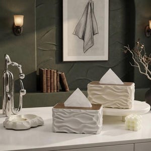 Peut inclure: Deux boîtes à mouchoirs rectangulaires avec un extérieur blanc texturé et ondulé et un couvercle supérieur lisse de couleur bois foncé. Chaque boîte contient un mouchoir blanc sortant par l'ouverture centrale au motif organique fluide.