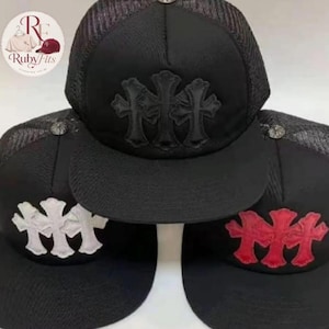 May include: Black trucker hats with a mesh back and a curved brim. Each hat features a three-cross emblem on the front in black, white, and red. The Ruby Fits logo is visible in the upper left corner.