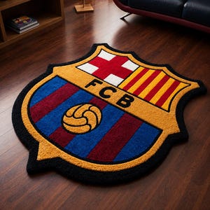 以下が含まれることがあります： 青、マルーン、黄色、赤、白のFCBロゴがあしらわれた盾形のラグ。中央にはサッカーボールのグラフィック、縦縞模様、そして黒い文字でFCBと描かれており、全体が太い黒の縁取りで囲まれています。
