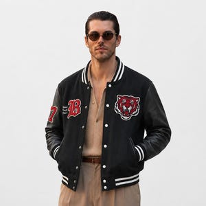 Könnte beinhalten: Eine schwarze Collegejacke mit Lederärmeln, weiß gestreiften Rippbündchen und Druckknöpfen. Auf der Brust befindet sich ein rot-weißes Tigerkopf-Abzeichen und ein roter Buchstabe B. Der Ärmel zeigt ein rotes Aufnäher mit der Zahl 17.