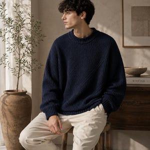 Puede incluir: Un suéter de manga larga en color azul marino oscuro con textura de punto acanalado y cuello redondo, combinado con pantalones de color beige claro. El suéter presenta un sutil patrón de punto diagonal en el frente, mangas largas y corte holgado.