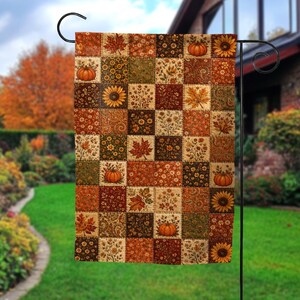 May include: A rectangular garden flag featuring a patchwork design of autumn-themed squares. The pattern includes illustrations of orange pumpkins, yellow sunflowers, brown maple leaves, and various floral motifs in shades of rust, gold, and green.