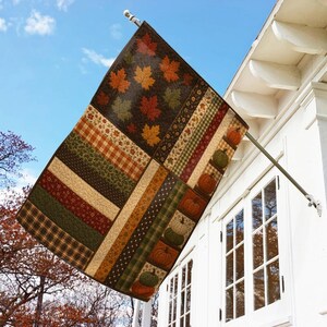 May include: A rectangular outdoor flag featuring a patchwork design of autumn-themed patterns, including orange, red, and green maple leaves, plaid stripes, and a vertical border displaying a series of small pumpkins in various fall colors.