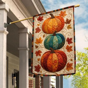 May include: A rectangular garden flag featuring a vertical stack of three pumpkins in orange, teal, and red, decorated with intricate floral patterns and surrounded by scattered autumn leaves in shades of red, orange, and yellow on a cream background.